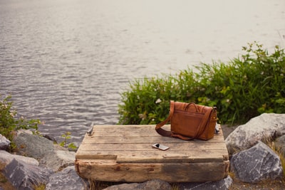棕色皮革crossbody包在水附近的布朗木板
